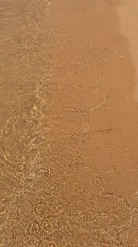 Golden beach waves gently lapping on sandy shoreline creating ripples in sunlight