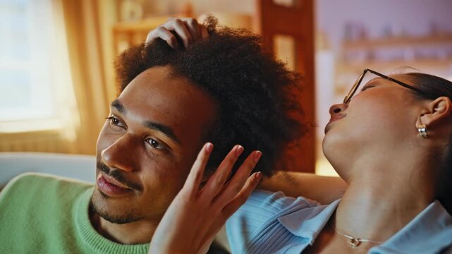 Woman ruffling boyfriend hair sofa closeup. Multiracial couple relaxing home.