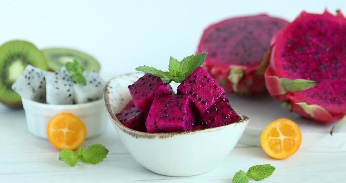 Woman adding mint to cut pitahaya at white table, closeup