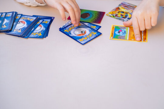 Young enthusiast Child holding Pokemon card, Collecting trading cards with Pokeball logo on white table, close up hands playing, sorting trading card game, Battle with friends, childhood Fan Culture