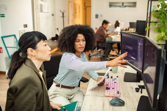 Two women reviewing design on dual monitors in office