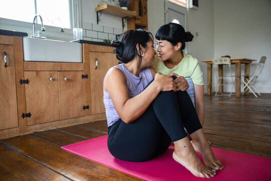Two women nuzzle on a yoga mat at home