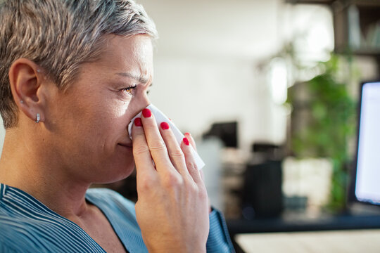 Woman wiping tears with tissue at office desk