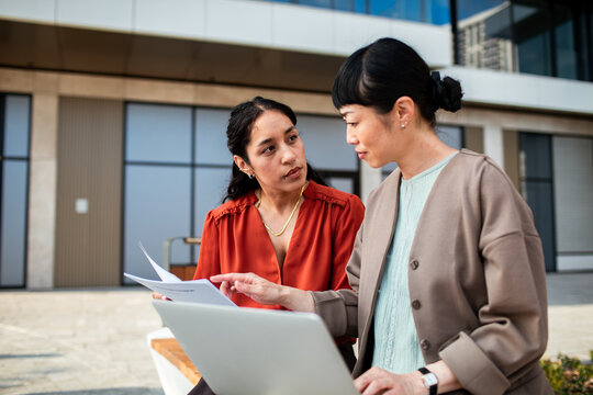 Two coworkers discussing paperwork with a laptop outdoors