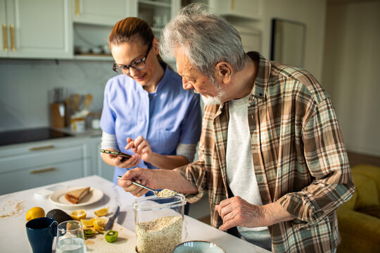Caregiver helps senior man prepare oatmeal in home kitchen