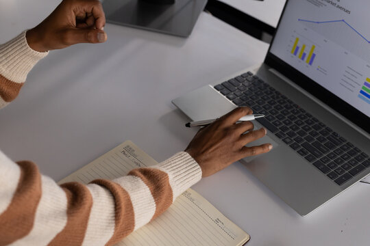 African American man in striped sweater working at desk with laptop charts, notebook and pen