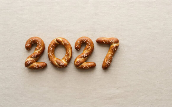 Pretzel number 2027 shaped from baked dough with salt on textile background representing future year celebration and culinary typography concept