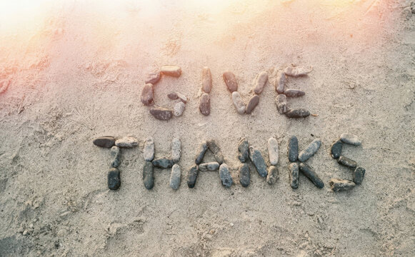 Give Thanks message spelled with beach pebbles on sand for Thanksgiving holiday concept design