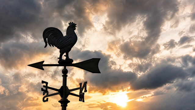 Vintage rooster weather vane silhouette against dramatic sunset sky, metal weathercock wind indicator, rustic weather instrument at golden hour