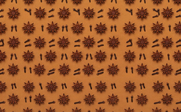 Star anise and clove spices arranged in a repeating pattern on an orange background for culinary design and food concepts