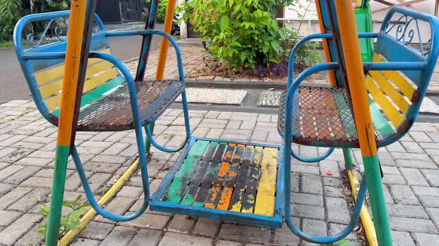 Old weathered outdoor playground swing set with dual facing seats made from metal pipes, showing aged surfaces and a nostalgic recreational structure