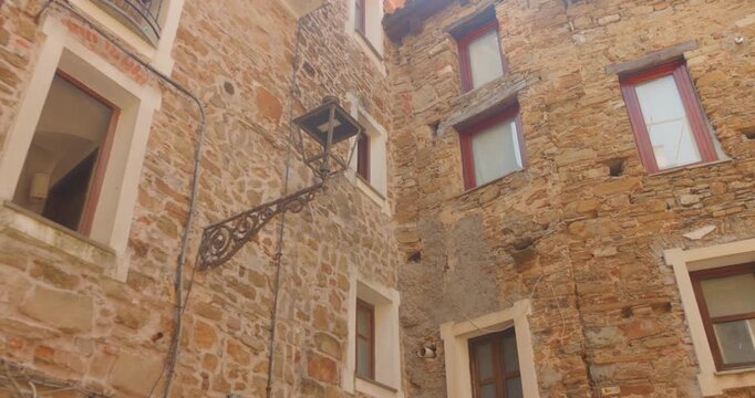 Weathered stone facades, shuttered windows and an ornate iron lantern fill a courtyard in medieval Perinaldo town, establishing backdrop, minimal people