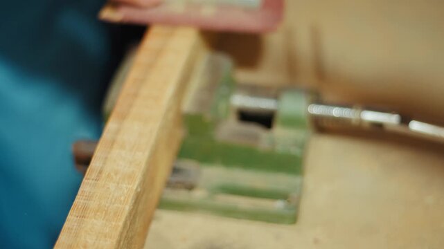 Close-up of a craftsman using a red sanding block to smooth a wooden plank by hand in a workshop. Authentic DIY woodworking footage for craft, carpentry and maker projects