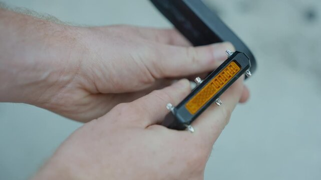 Hands inspecting a gravel bike pedal with reflector and metal pins.