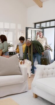 Vertical video: Diverse group arriving with rolling suitcase entering home petting dog reuniting