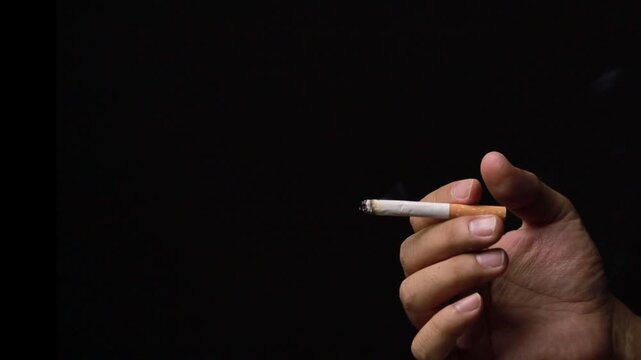 Hand flicking ash from a lit cigarette in the dark