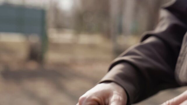 Person hand manipulates coiled brown leather strap with white stitching focusing on texture and movement of hands and straps in outdoor setting. background remains softly blurred throughout
