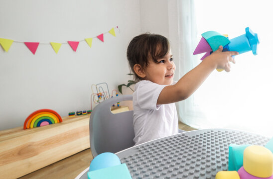 Happy toddler girl playing with airplane foam toy at kindergarten classroom - Early childhood education and creative play concept - Focus on child face