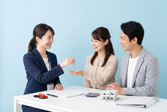 不動産会社の女性スタッフから家の鍵を受け取る夫婦 マイホーム購入や契約成立のイメージ写真