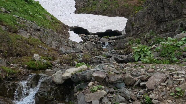 Melting snow cave and crystal clear mountain stream flowing over rocks in spring