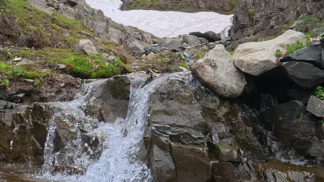 Fresh mountain stream cascading over rocks with melting snow background in spring