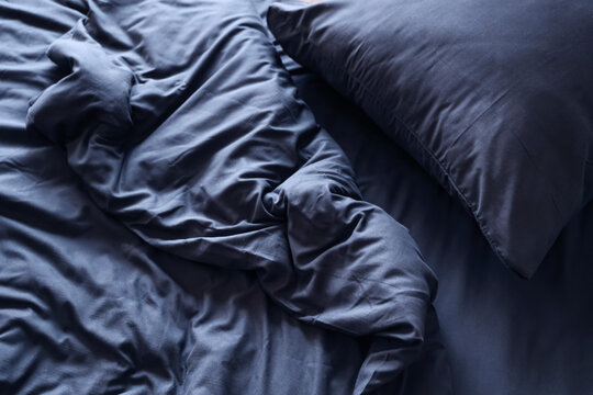 Insomnia and sleep disorder, messy dark blue bed sheets with unmade pillow in morning light