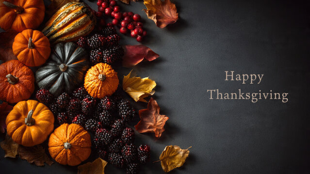 Autumn harvest arrangement of pumpkins blackberries and colorful fall leaves on a dark background