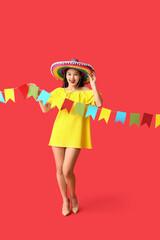 Obraz premium Festa junina celebration and cultural festival, happy young woman wearing a colorful sombrero holding traditional party bunting on a red background
