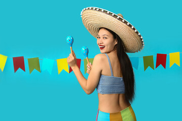 Obraz premium Cinco de mayo celebration and mexican culture, happy young woman wearing a sombrero and holding maracas with festive party flags on blue background