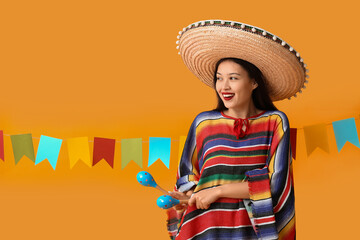 Obraz premium Cinco de mayo celebration, happy young woman wearing traditional mexican poncho and sombrero holding maracas for festive party event on orange background