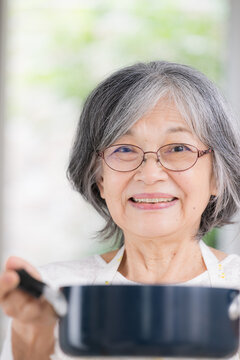 自宅で料理をする元気な日本人の高齢女性、自炊、家事、健康的な食生活、健康寿命、自立したシニアの暮らしカメラ目線の笑顔クローズアップ