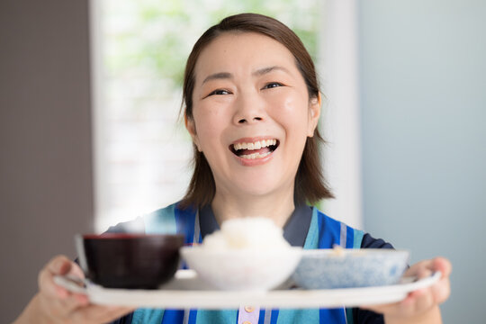 食事を配膳する笑顔の介護スタッフ、訪問介護、家事代行で食事を提供のホームヘルパーイメージカメラ目線