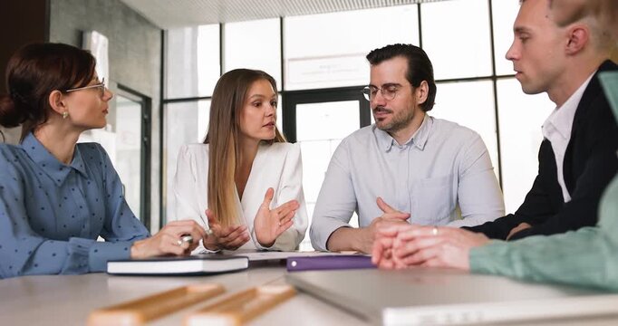 Confident female entrepreneur speaking at round table meeting with business partners team in modern office expressing idea explaining strategic concept presenting project plan for group discussion