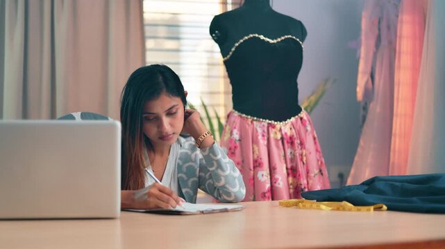 Female fashion Design professional sketching garment ideas and planning a dress design project at a studio worktable.