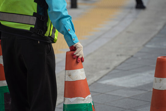 Traffic controller holding an orange traffic cone on the street