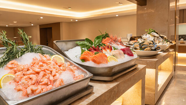 A variety of fresh chilled seafood including shrimp, sashimi, shellfish arranged on ice for a buffet display in a modern restaurant.
