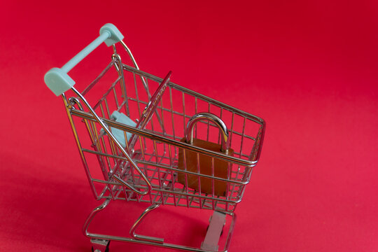 Small shopping cart locked with padlock on red background. Symbolizes security, online shopping restrictions or payment hold. Could use in finance, e-commerce, or retail security concepts