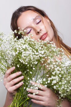 Woman holds Baby's Breath flowers near face with eyes closed. Serene, dreamy expression concept