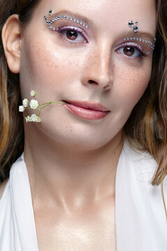 Close beauty portrait of young woman with freckles holding brunch of gypsophila flowers between her lips