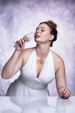 Woman in white evening gown raises wine glass filled with pearls. Luxury female portrait.