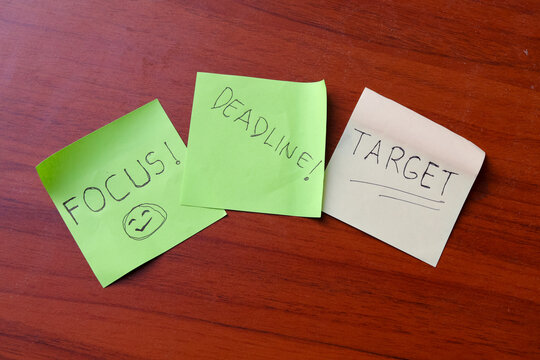 Top view of colorful sticky notes with handwritten words focus deadline and target placed on wooden office desk