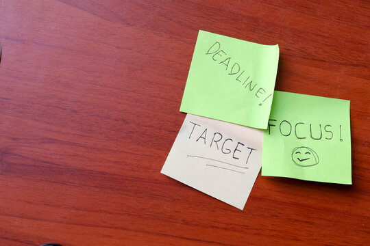 Top view of colorful sticky notes with handwritten words deadline target and focus on wooden desk with copy space