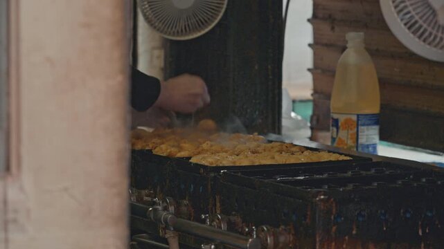 4K Chef turning golden takoyaki octopus balls on traditional iron pan at street food stall.