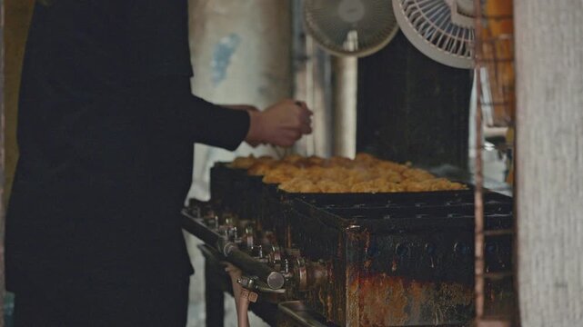 4K Chef turning golden takoyaki octopus balls on traditional iron pan at street food stall.