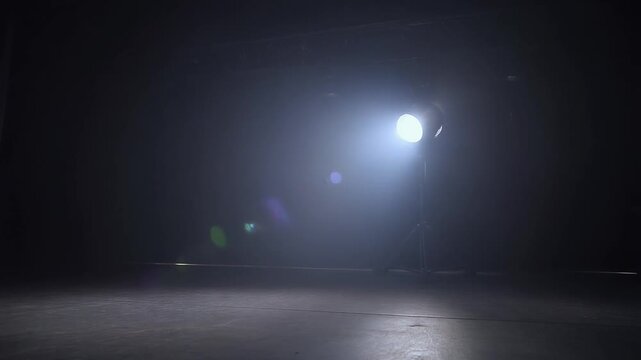 Studio spotlight shining brightly on an empty dark stage with smoke and lens flare