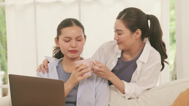 A caring woman brings a hot drink and gives a relaxing shoulder massage to her partner working on a laptop.