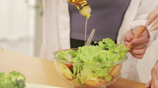 Close up of hands pouring olive oil over a fresh healthy salad in a glass bowl and mixing it on a wooden table.	