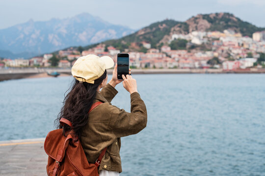 Young female traveler taking photos and enjoying the scenic view of the fishing village along the coast at Shazikou in Qingdao