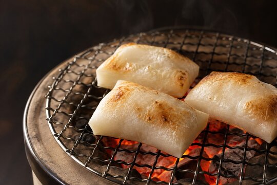 Japanese kiri mochi grilling over glowing charcoal with golden toast marks, cozy traditional winter food