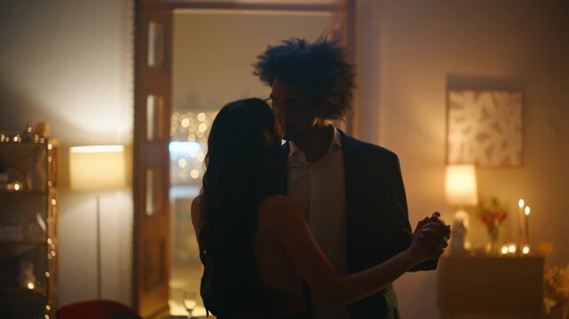 Lovers slow dancing candlelight evening apartment. Multiracial pair embracing.